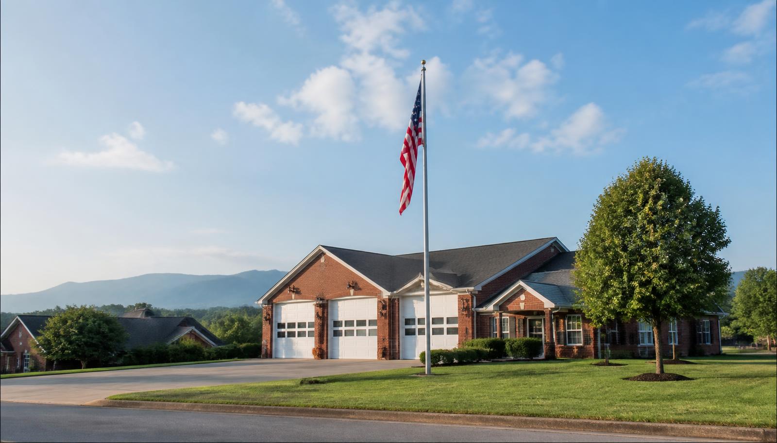 Brick Wilkesboro fire station with white garage doors and an American flag in front of the Blue Ridge mountains